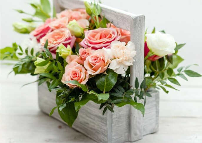 cvetochnaya kompoziciya iz roz i zelenykh listev v derevyannoj beloj korobke s ruchkoj