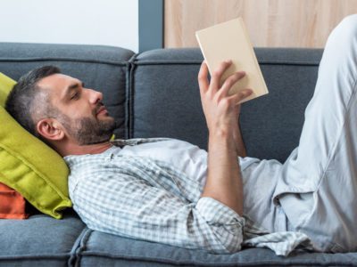 Что подарить мужчине на 55 лет - оригинальные идеи в готовых списках, мужчина лежит на диване и читает книгу