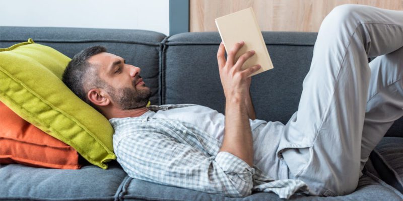 Что подарить мужчине на 55 лет - оригинальные идеи в готовых списках, мужчина лежит на диване и читает книгу